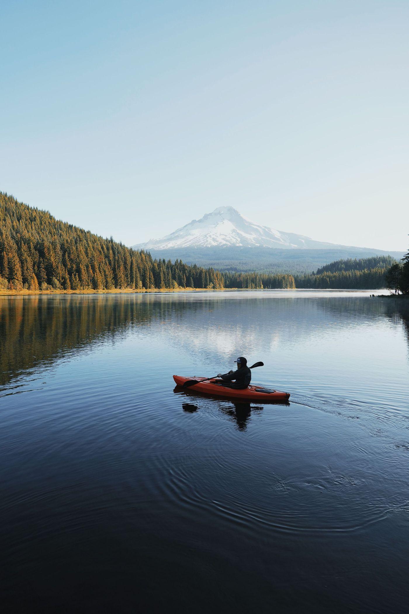A kayaker paddling across a lake surrounded by forest below a snow-capped mountain